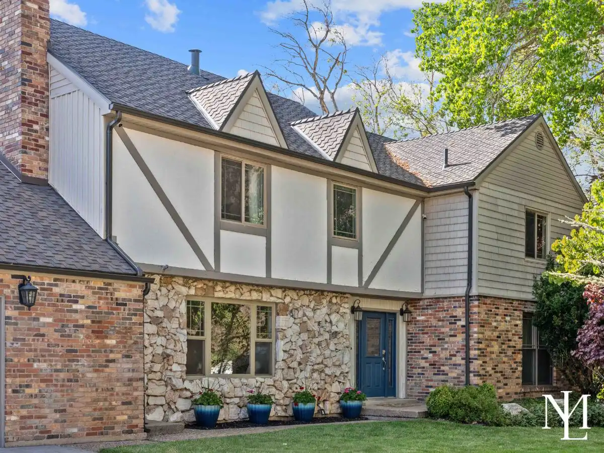 Front exterior of a Tudor-style brick, stone, and stucco home in Uintah, Utah featuring a blue front door, manicured landscaping, and mature shade trees.