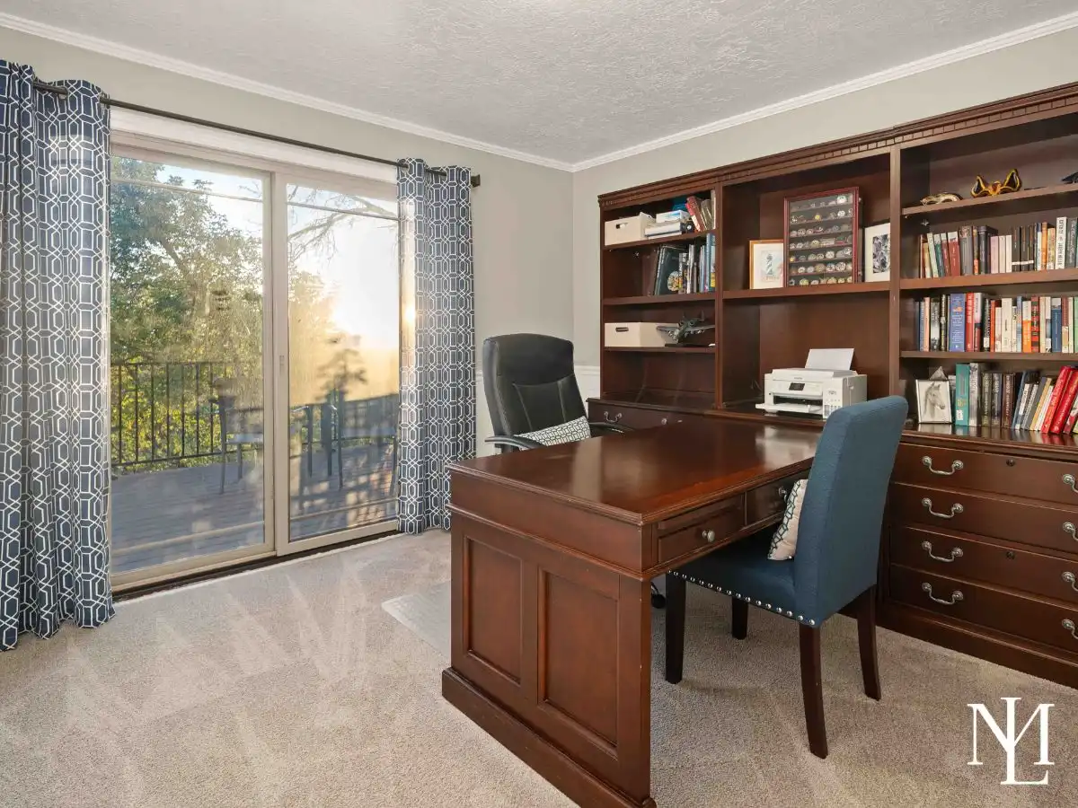 Home office with built-in wood bookcases, dedicated workspace, plush carpet, and sliding glass door opening to a private deck.