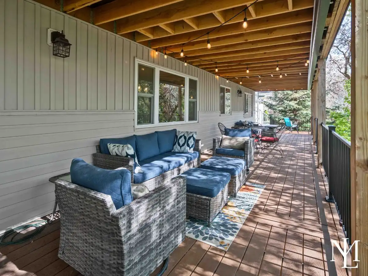 Covered back deck with outdoor seating, wood decking, string lights, and a quiet tree-lined backdrop for relaxing or entertaining.