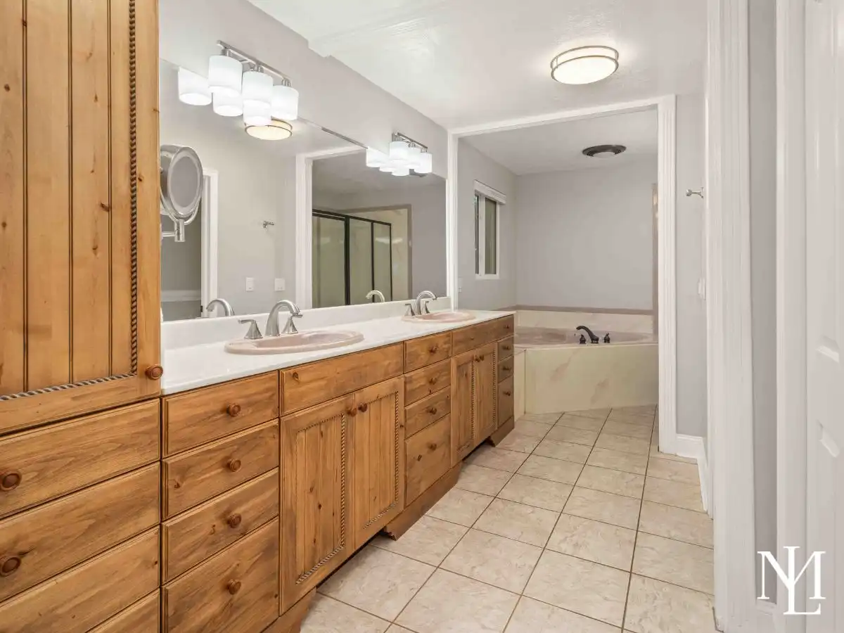 Primary bathroom with extended double vanity, abundant cabinet storage, tile flooring, and a large soaking tub tucked into the rear of the suite.
