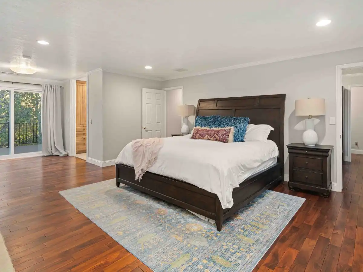 Spacious primary bedroom with hardwood flooring, large sleeping area, private balcony access, and room for a sitting area.