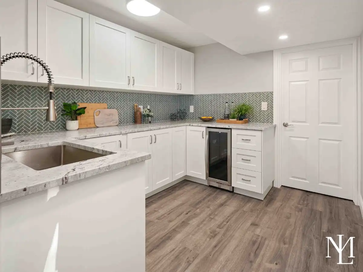 Lower-level kitchenette with white cabinetry, stone-look counters, beverage fridge, modern backsplash, and durable wood-look flooring.