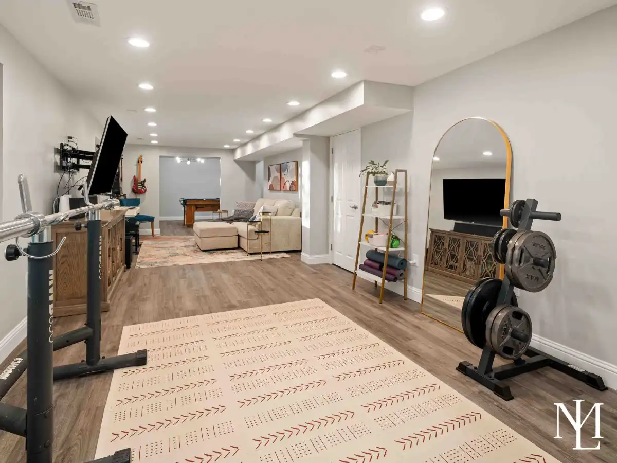 Finished lower level with exercise space, lounge area, large wall-mounted TV, and flexible room for recreation, workouts, or entertaining.