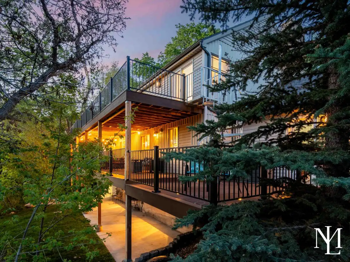 Rear exterior of the home at dusk featuring multiple decks, warm outdoor lighting, mature evergreens, and a secluded wooded setting.