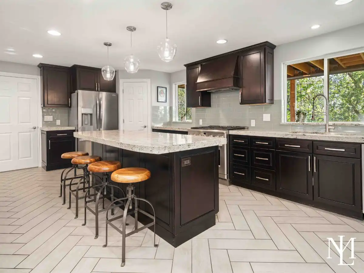 Updated kitchen with dark cabinetry, granite island, stainless steel appliances, light tile flooring, and windows overlooking the wooded backyard.
