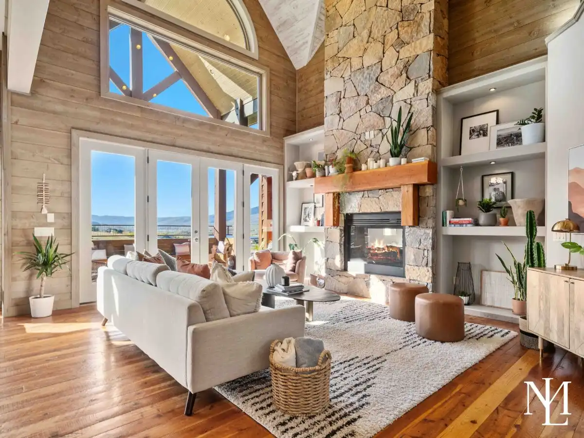 Vaulted great room with floor-to-ceiling stone fireplace, built-ins, and glass doors opening to reservoir-view deck in Huntsville, Utah.