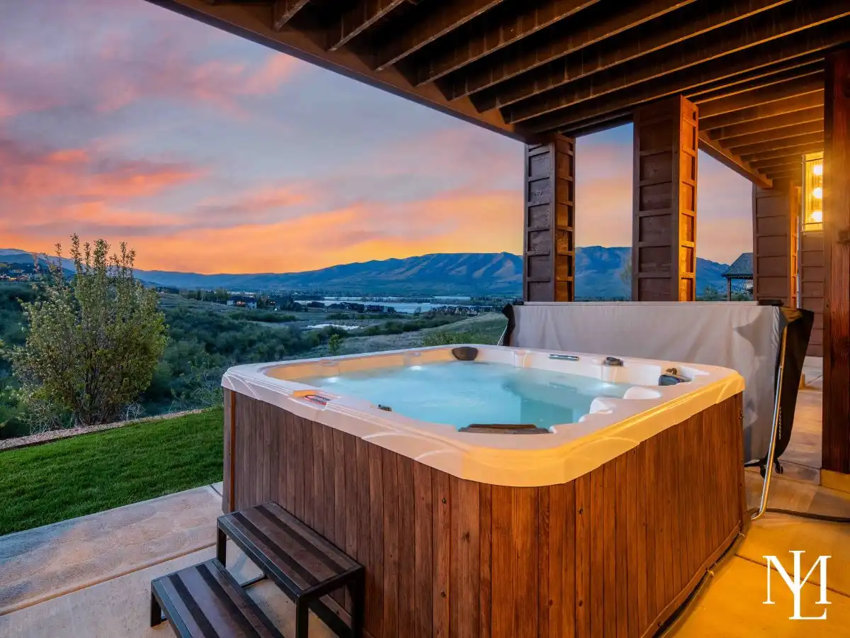 Outdoor hot tub at sunset with glowing sky, valley backdrop, and sweeping views toward Pineview Reservoir in Huntsville, Utah.