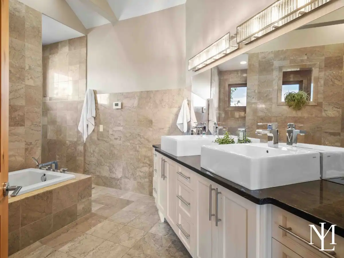 Spa-inspired primary bathroom with double vessel sinks, soaking tub, and full-height stone tile in custom mountain estate.