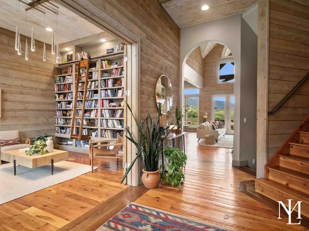 Warm wood-lined entry with wide-plank floors, staircase, and floor-to-ceiling library shelving in luxury Huntsville mountain home.