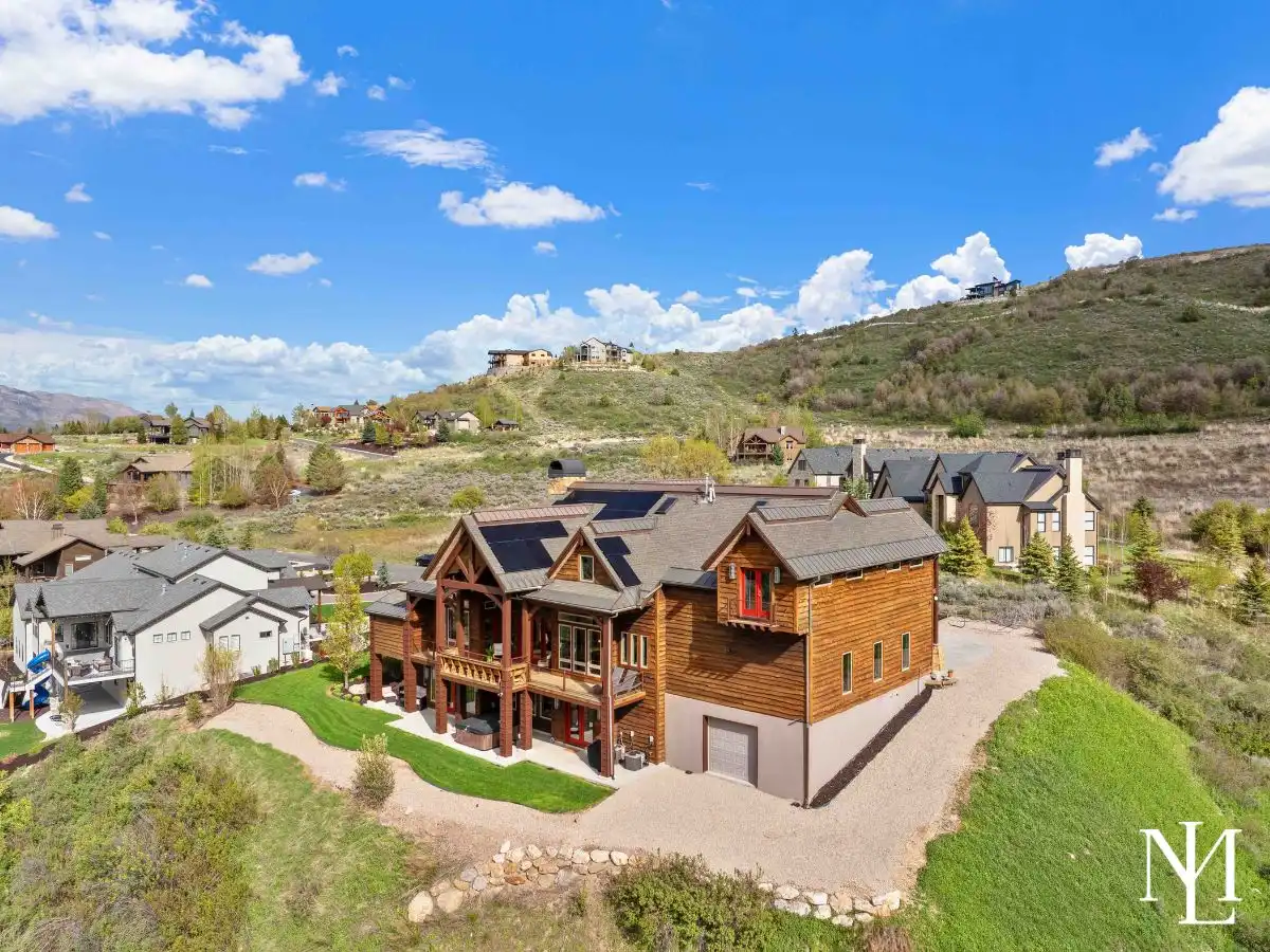Daytime aerial of luxury Huntsville mountain home with solar panels, expansive outdoor living, and hillside setting above Ogden Valley.