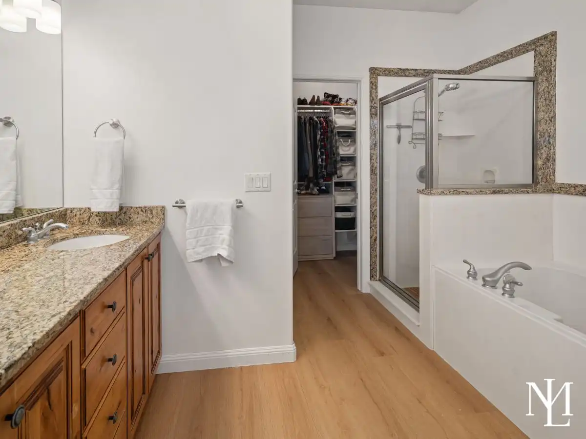 Primary bathroom with granite vanity, soaking tub, glass shower, and walk-in closet access.
