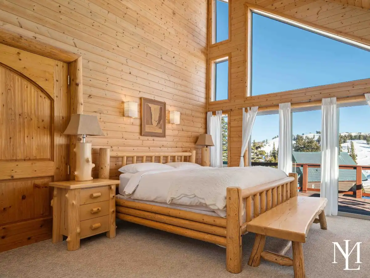 Primary bedroom with log bed, vaulted ceiling, and tall windows overlooking snowy mountain scenery.