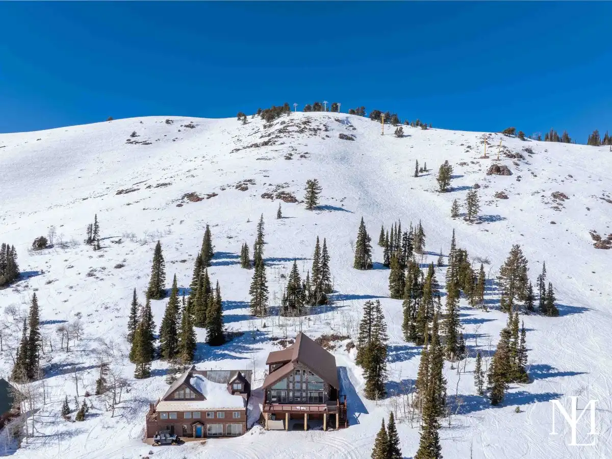Drone view of an Eden, Utah mountain cabin below snow-covered ski runs and chairlifts.