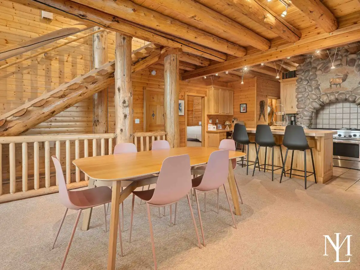 Open dining area with exposed log beams and kitchen bar seating in a rustic mountain cabin.