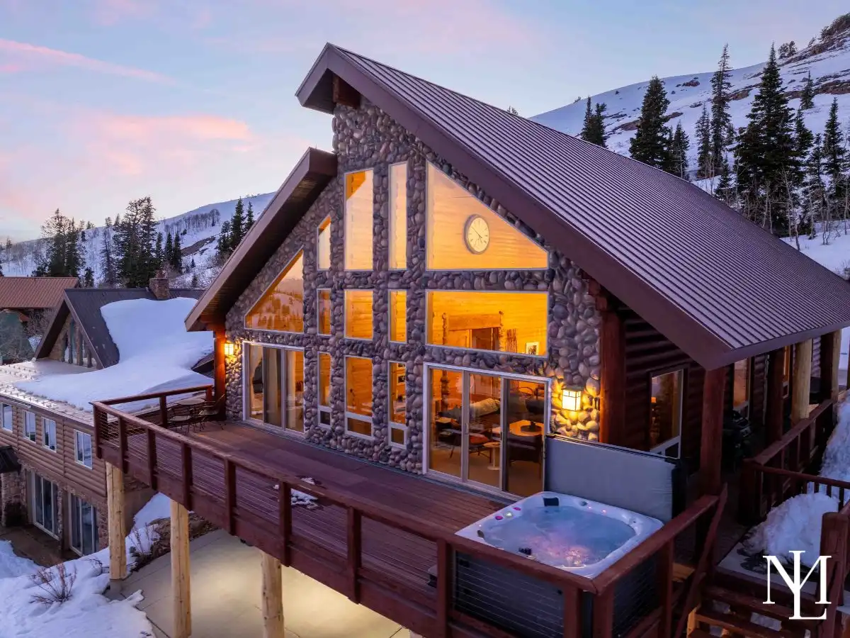 River-rock and timber ski cabin exterior with wraparound deck and private hot tub, nestled in snowy Eden, Utah.