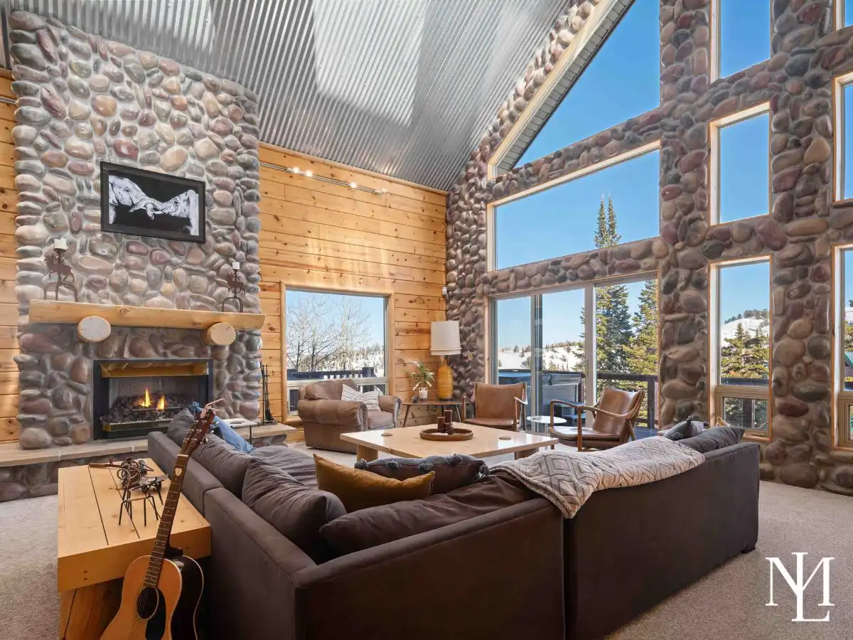 Vaulted living room with stone fireplace, oversized windows, and mountain views in an Eden, Utah ski cabin.
