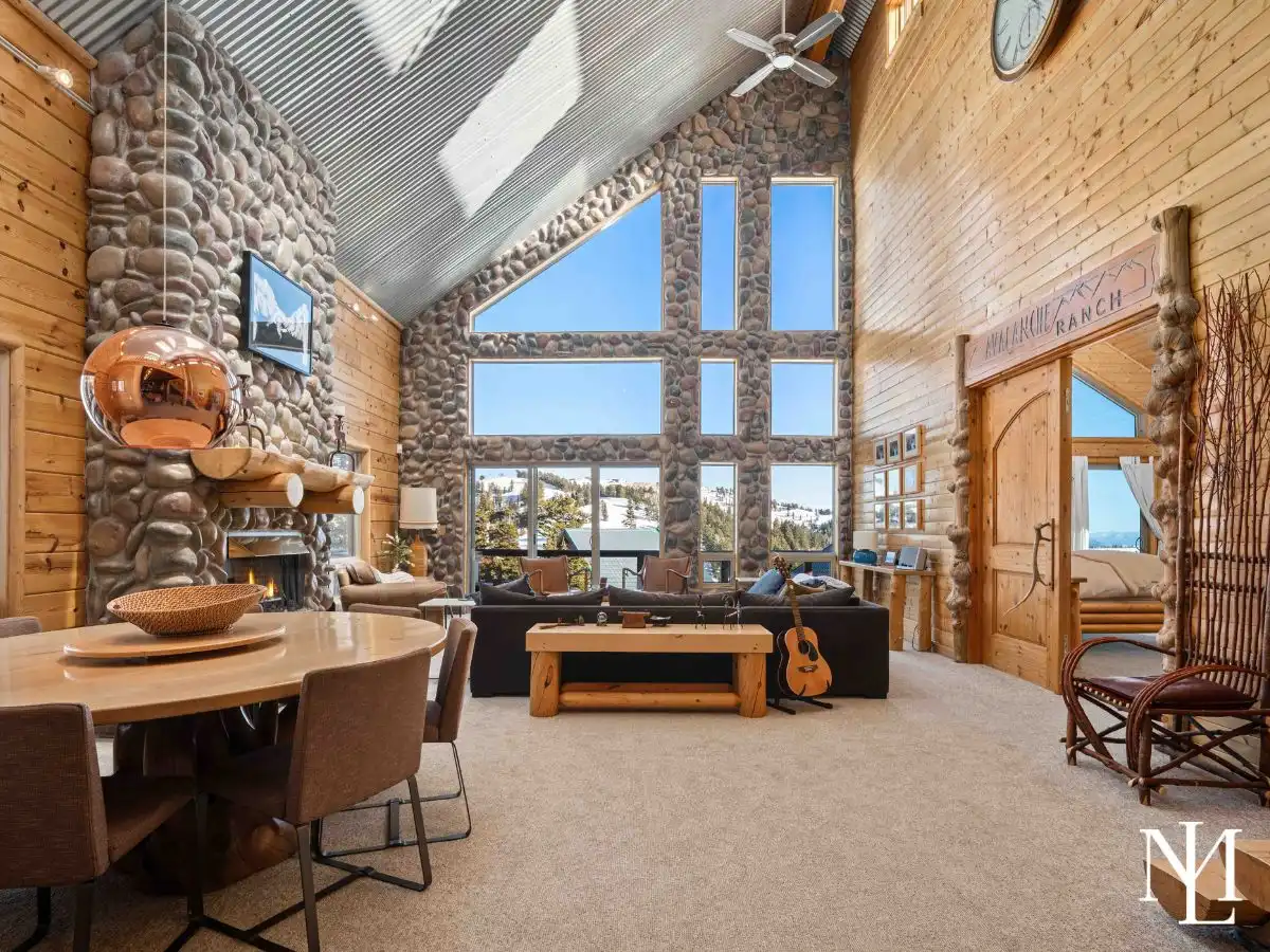 Great room with floor-to-ceiling windows, stone fireplace, and dining area in a rustic Eden, Utah cabin.