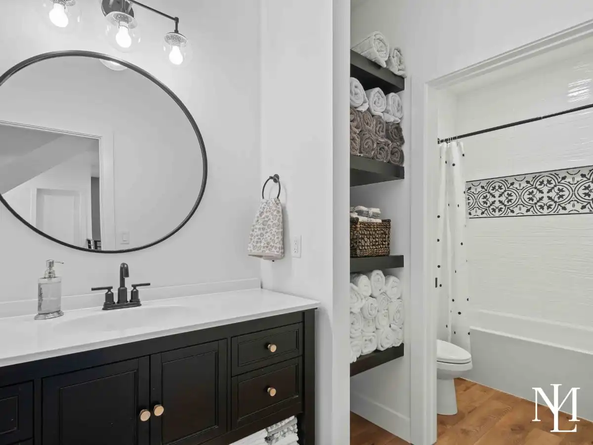 Bathroom with black vanity, round mirror, built-in shelving, and tiled tub-shower combo.
