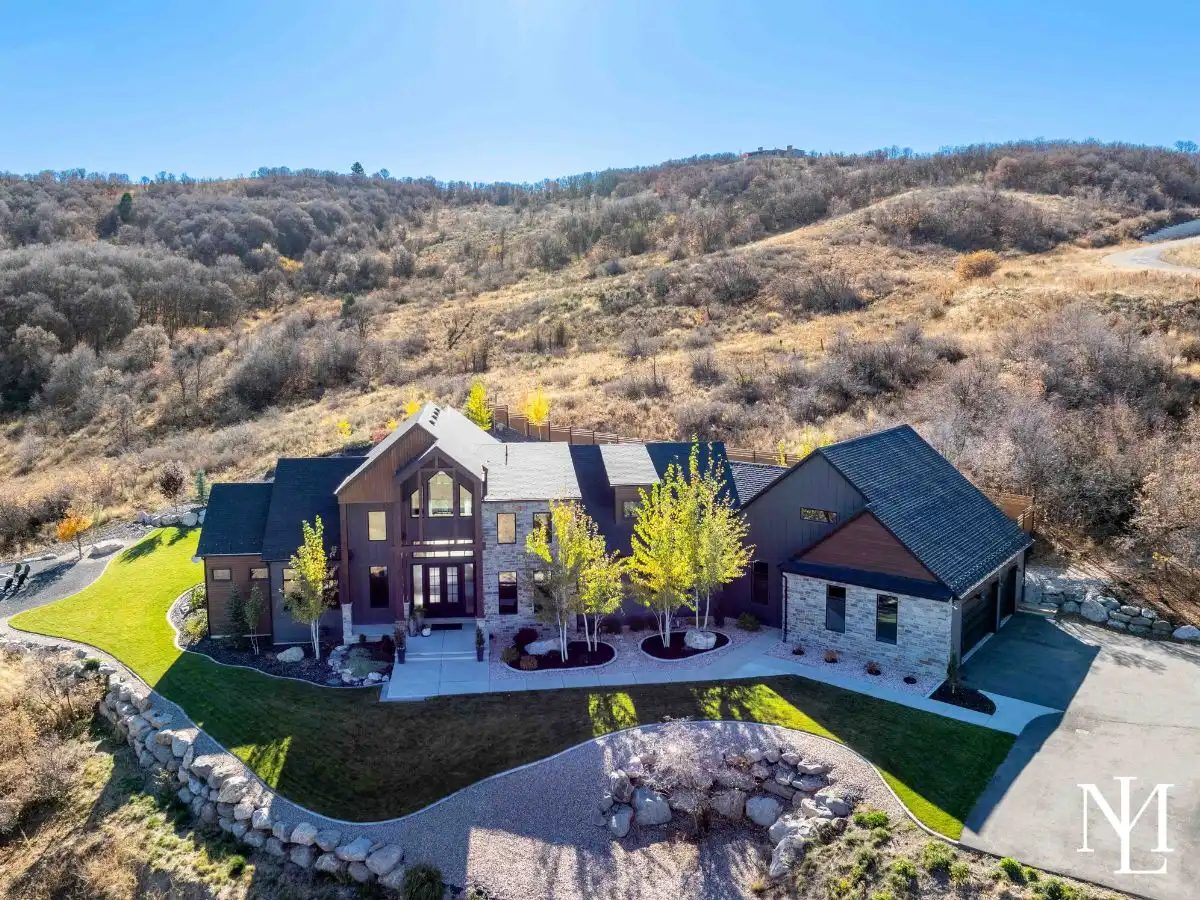 Aerial front view of custom mountain home surrounded by foothills and landscaped grounds.