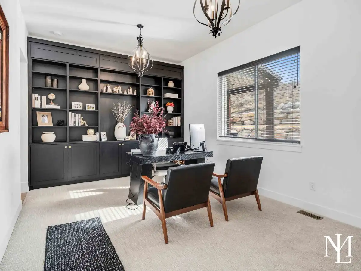 Home office with custom built-in shelving, large window, and modern lighting.