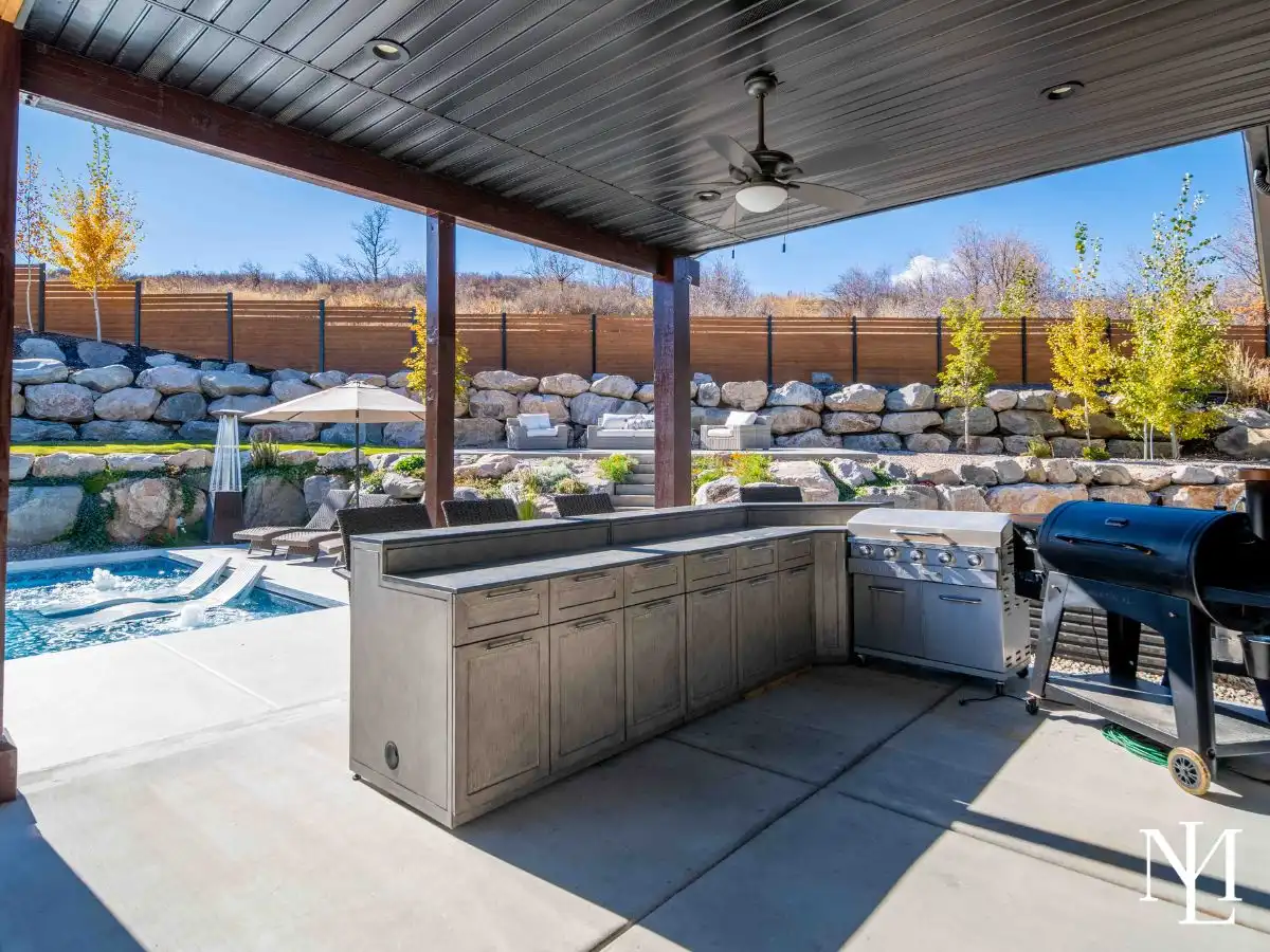 Covered patio with outdoor kitchen, grill, and views of the pool and landscaped yard.