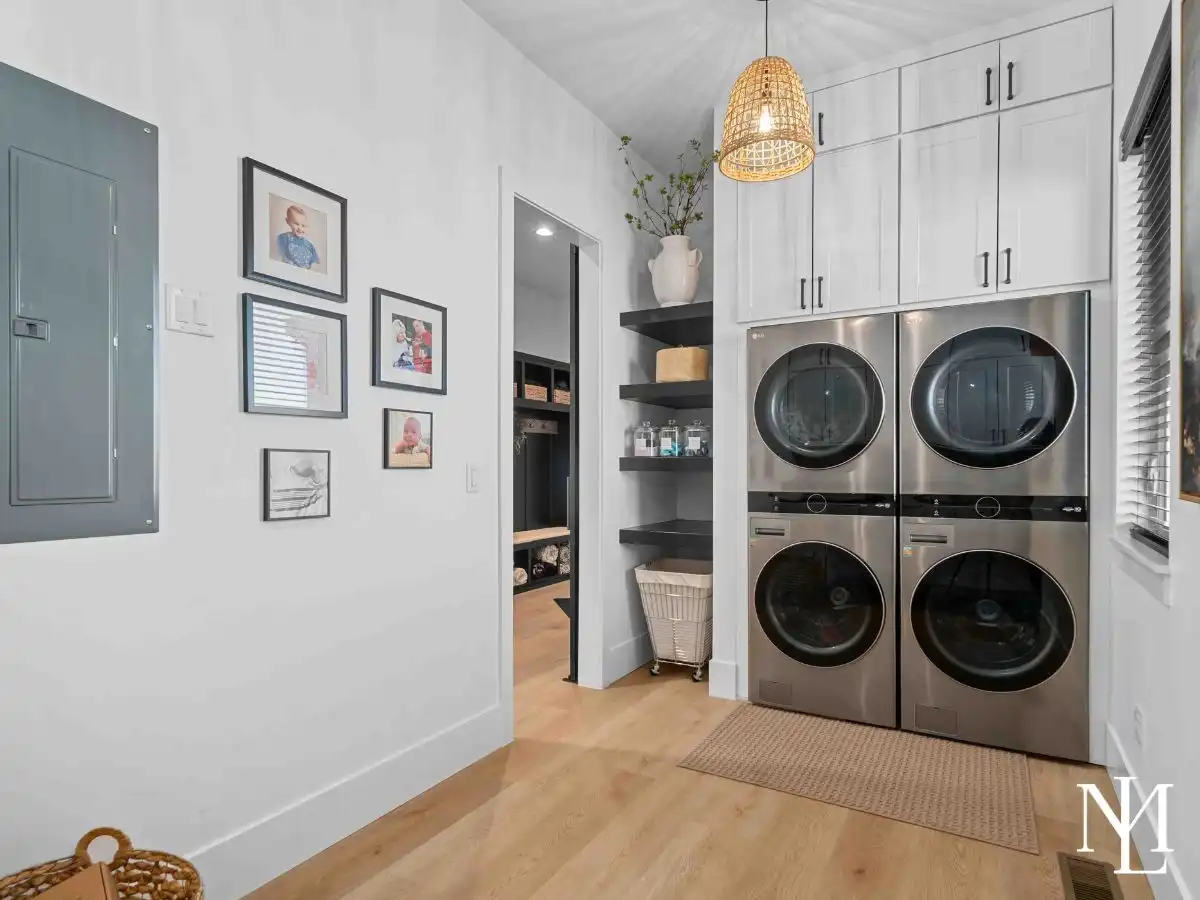 Laundry room with stacked stainless steel washer and dryer, built-in cabinetry, and open shelving.