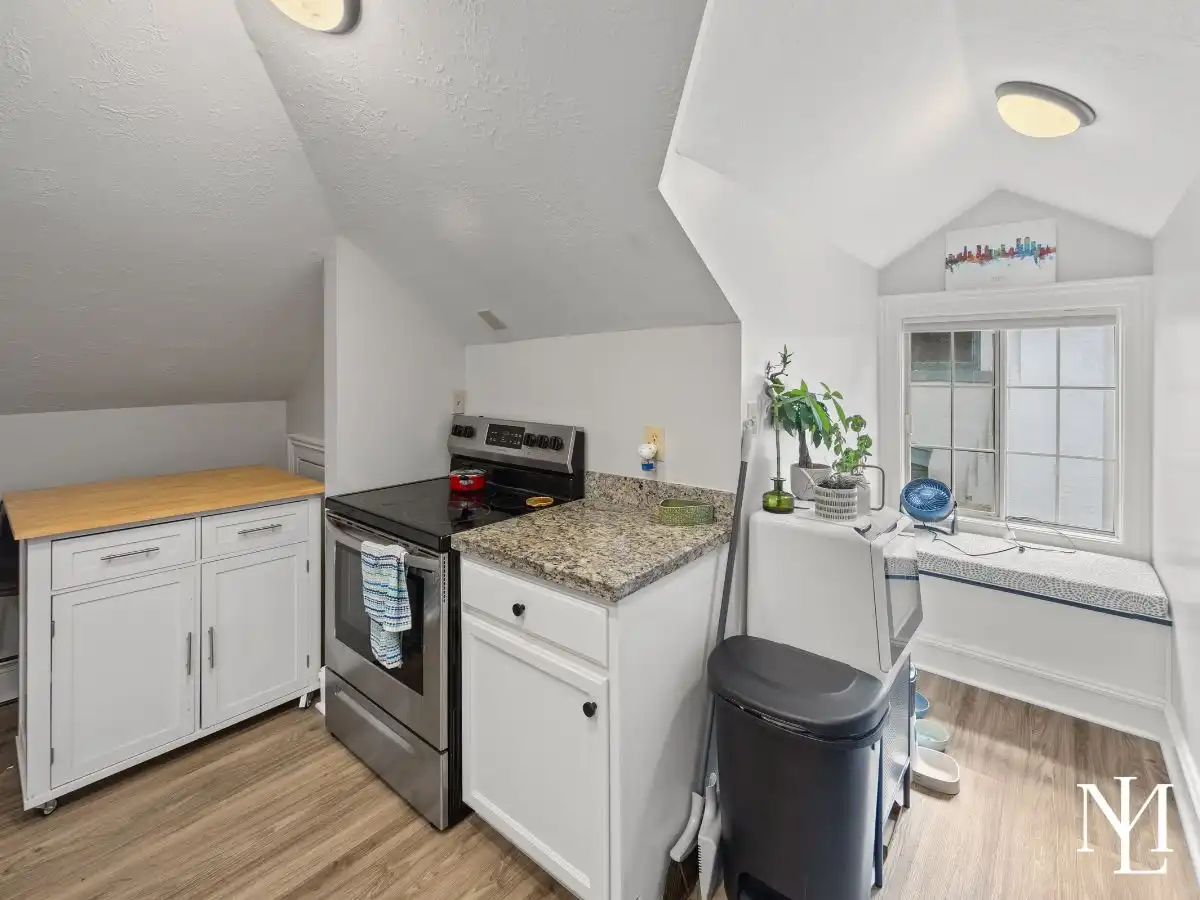 Compact kitchenette in Avenues triplex with white cabinetry, granite countertop, stove, and window seat