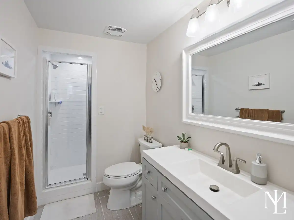 Updated bathroom in Avenues home with white vanity, large mirror, tile shower, and neutral modern finishes