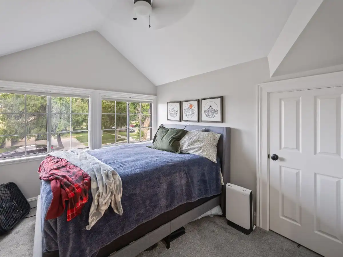 Upstairs bedroom with vaulted ceiling, large windows, carpet flooring, and cozy natural light