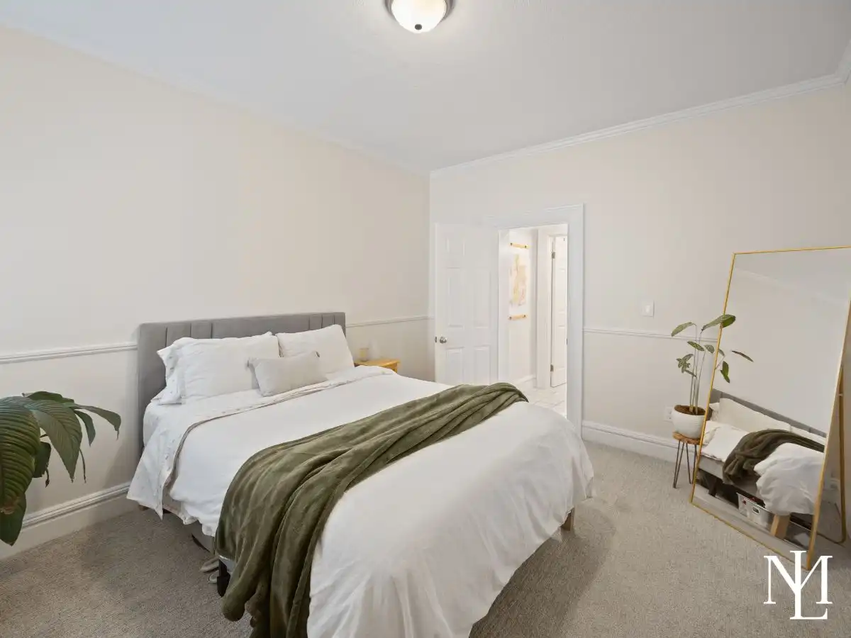 Neutral bedroom with carpet flooring, white bedding, full-length mirror, and clean finishes