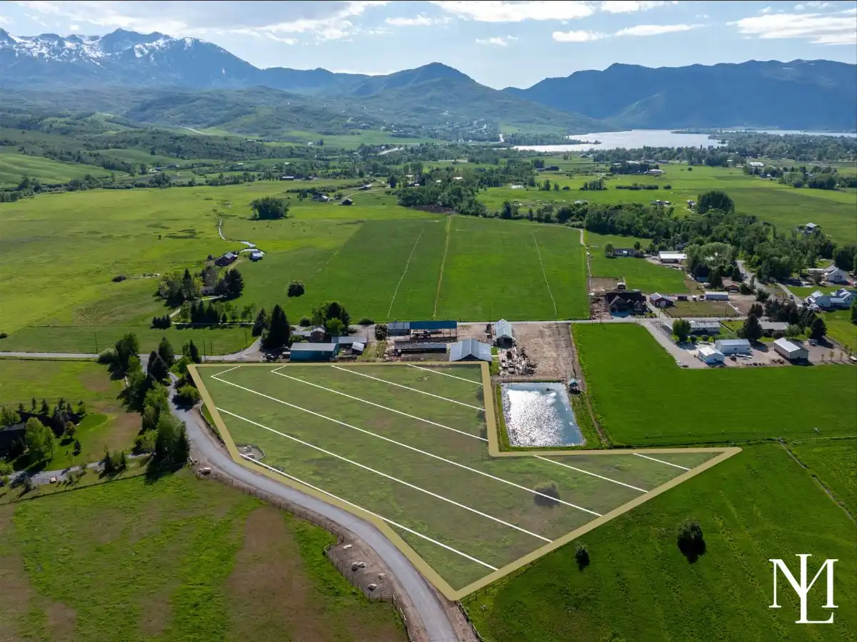 Wide aerial of subdivided land in Huntsville UT with outlined lot boundaries, irrigated fields, and Pineview Reservoir and mountains beyond.