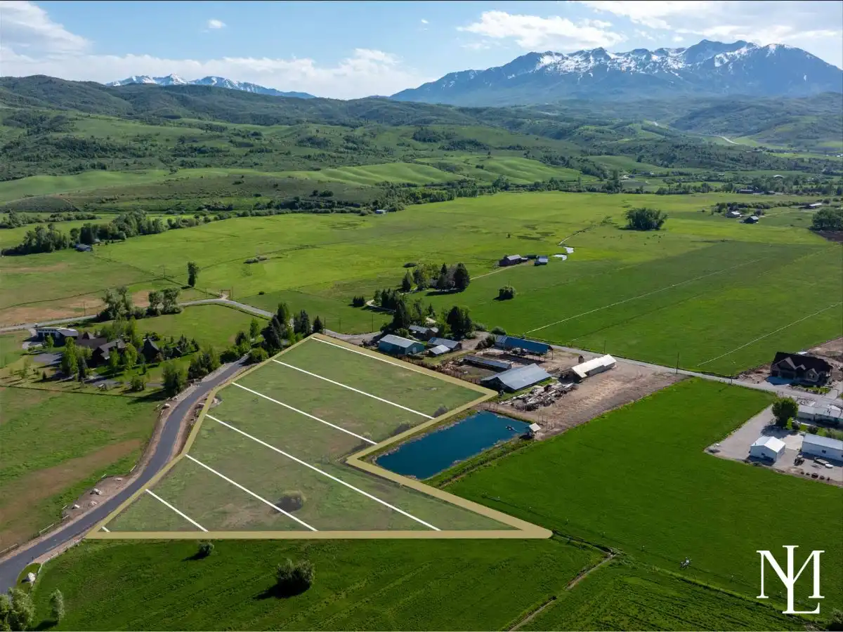 Drone view of open acreage with outlined building lots, pond nearby, and broad valley-and-mountain views in Huntsville, Utah.