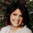 Emily Aulrich smiling professional portrait for Mountain Luxury with lilac flowers and greenery in the background