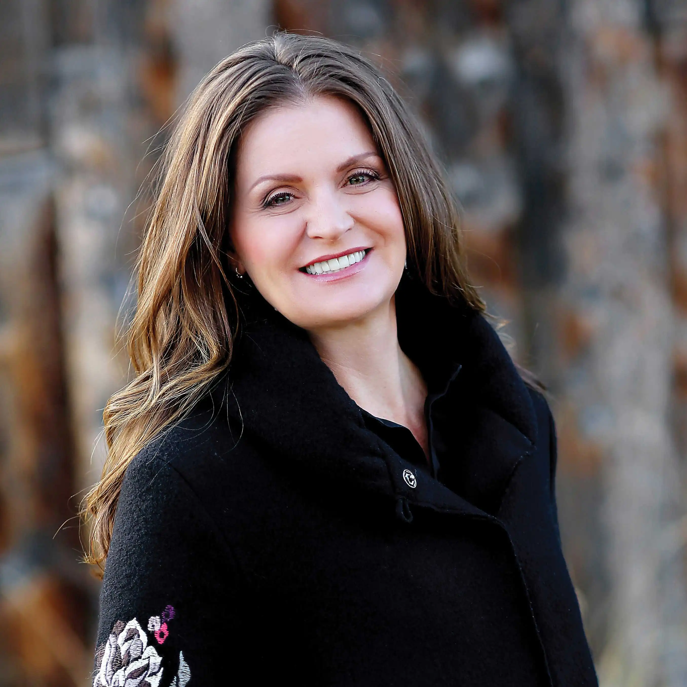 Brandi Hammon smiling for the camera in a black felt coat with embroidered flowers.