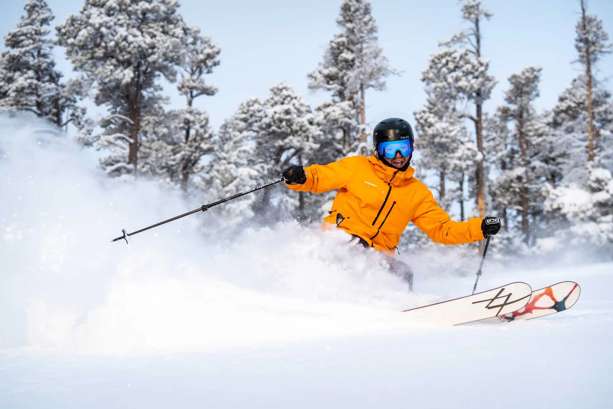 Skier carving fresh powder at Eldora Ski Resort in Nederland, Colorado, with snow-covered pines in the background.