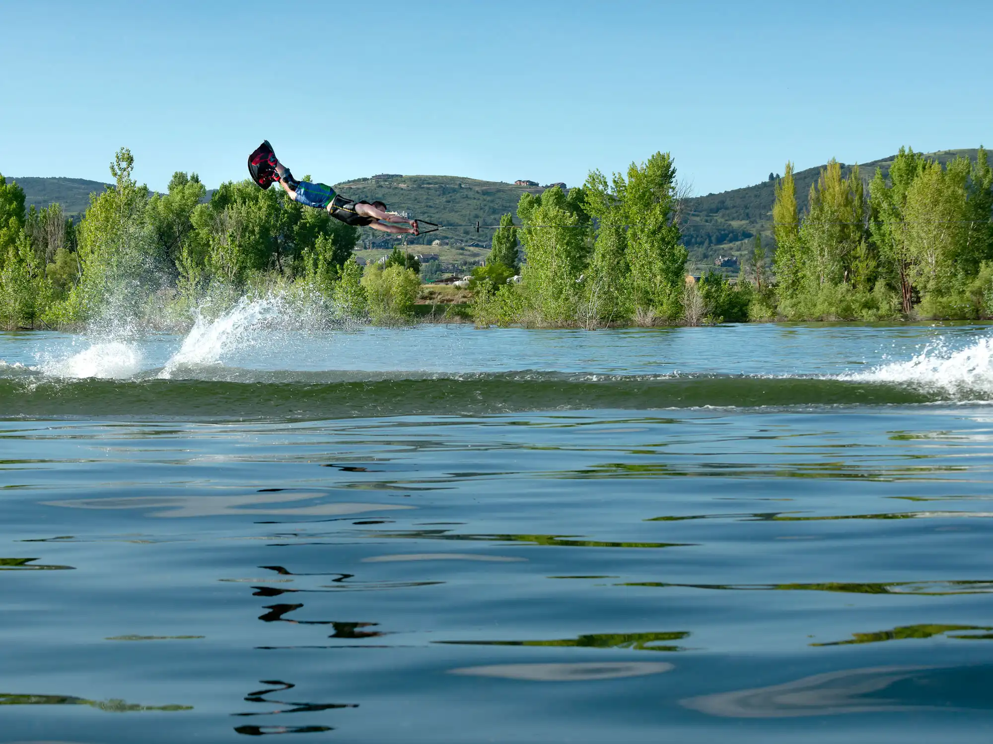Wakeboarder performing an aerial trick on Pineview Reservoir in Ogden Valley, Utah with mountain views and summer water recreation.