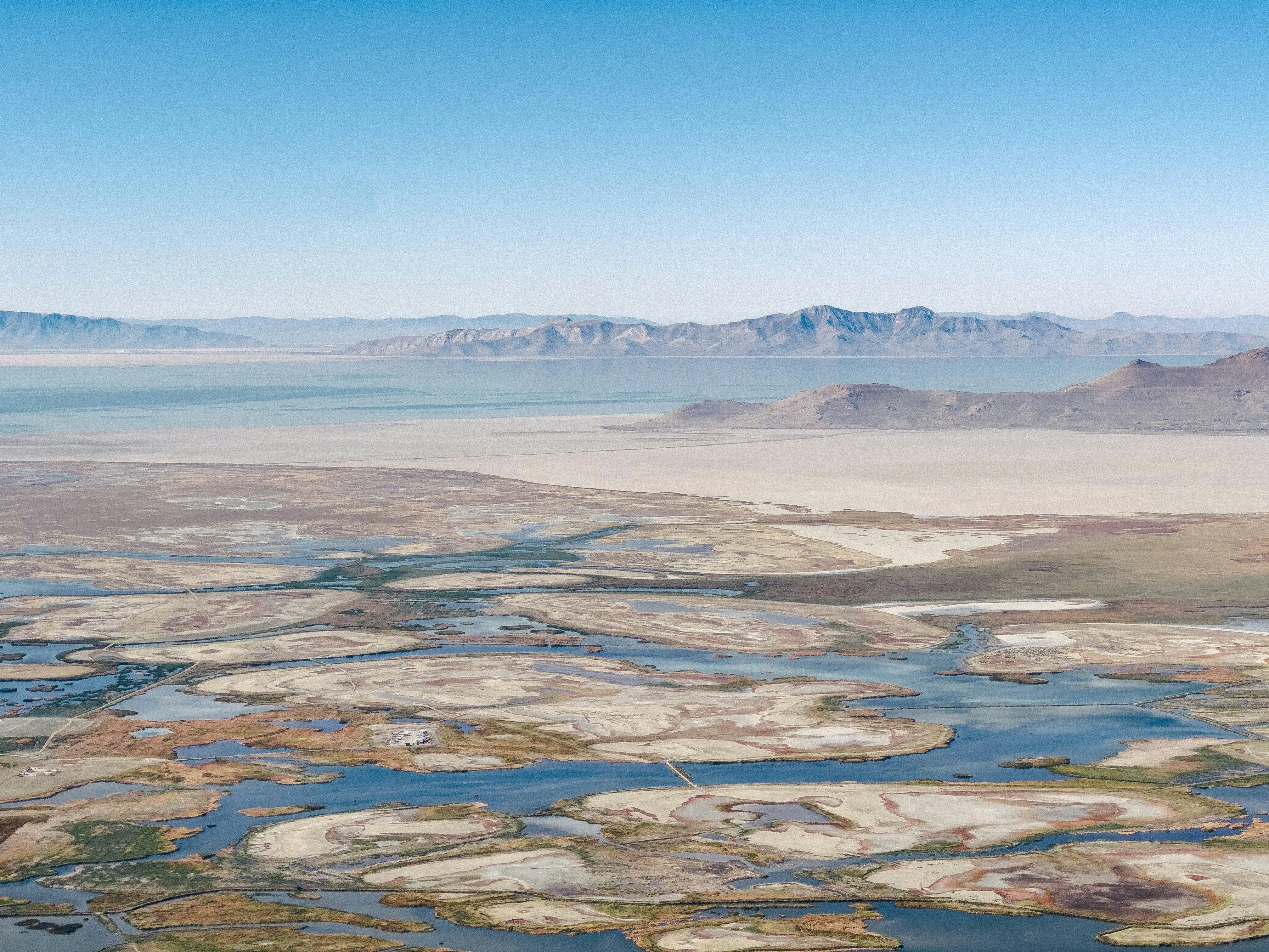 Aerial view of Great Salt Lake wetlands with exposed lakebed, shallow water channels, and desert mountains.