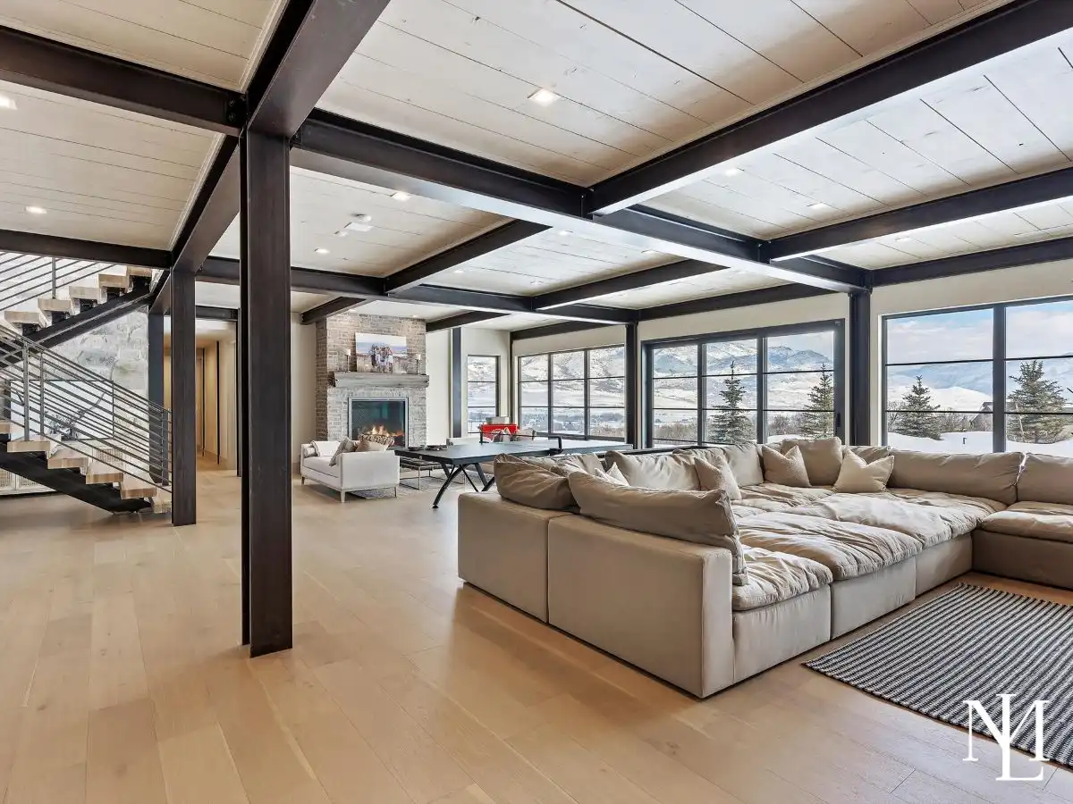 Open family room with exposed steel beams, oversized sectional sofa, fireplace, game table, and mountain views through large picture windows.