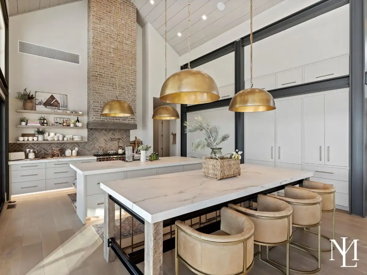 Luxury kitchen with double islands, brass pendant lighting, tall custom cabinetry, brick fireplace surround, and warm modern finishes.