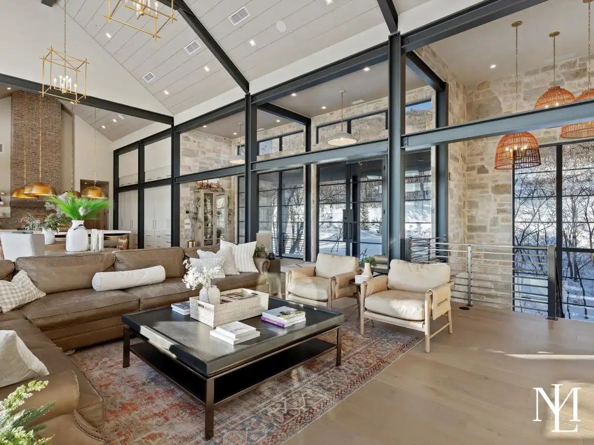 Open family room with exposed steel beams, oversized sectional sofa, fireplace, game table, and mountain views through large picture windows.