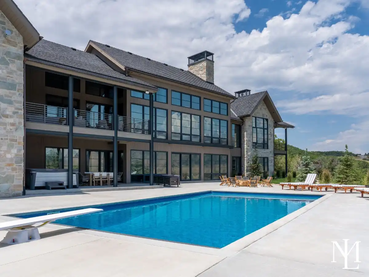 Large luxury home with expansive rear windows, covered patio, in-ground swimming pool, hot tub, and open mountain-view backyard.