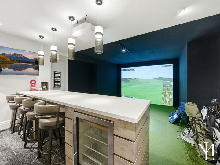 Indoor golf simulator with bar seating, beverage fridge, and entertainment space in custom Ogden Valley estate.