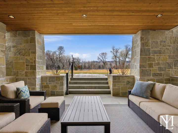 Covered outdoor lounge with stone columns, wood ceiling, and open views across the lawn in luxury Huntsville home.