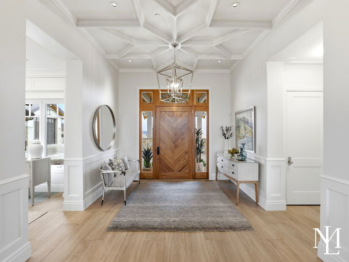 Bright entry foyer with chevron wood front door, coffered ceiling, and refined white millwork in luxury Huntsville home.