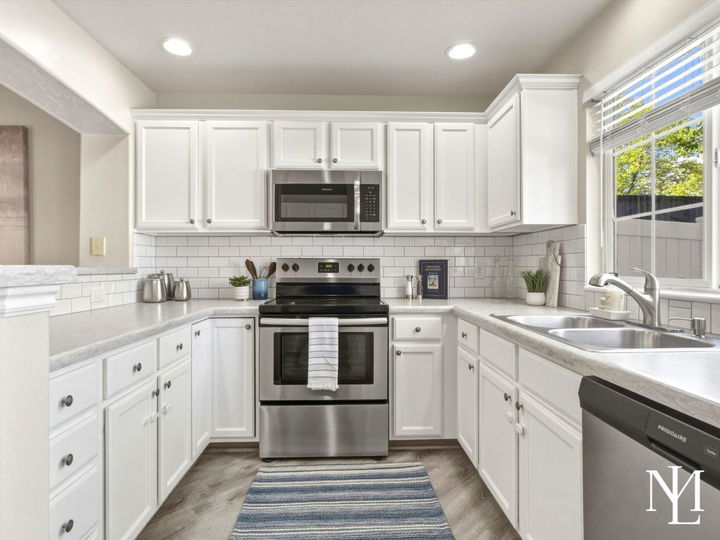 Updated white kitchen in Draper townhome with stainless steel appliances, subway tile backsplash, and window over the sink