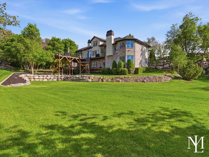 Rear exterior of Layton Utah home with large green lawn, mature landscaping, and elevated deck overlooking private yard.