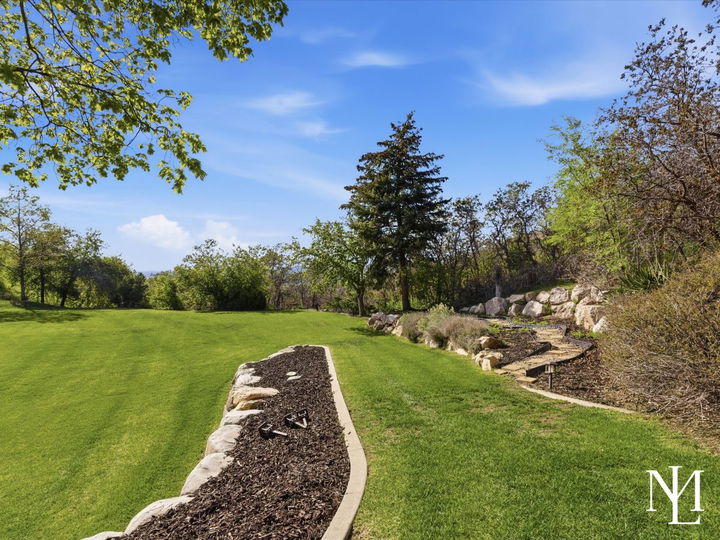 Private landscaped yard with stone-edged lawn and hillside garden path behind upper bench Layton home.
