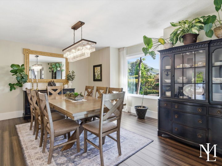 Elegant dining room with statement chandelier, large picture window, and warm wood flooring in luxury Layton residence.