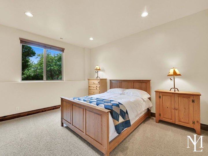 Lower-level bedroom in Eden Utah mountain home with wood bed frame, neutral carpet, recessed lighting, and window views