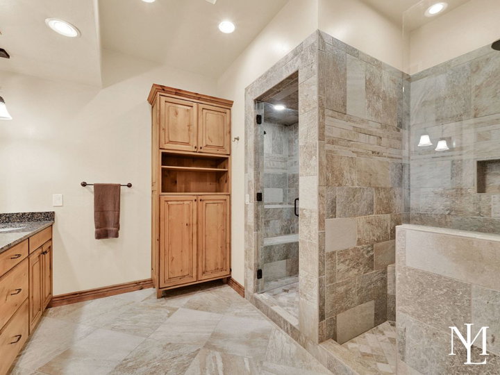 Spacious bathroom in Eden Utah home with tile walk-in shower, soaking tub, custom cabinetry, and natural stone finishes